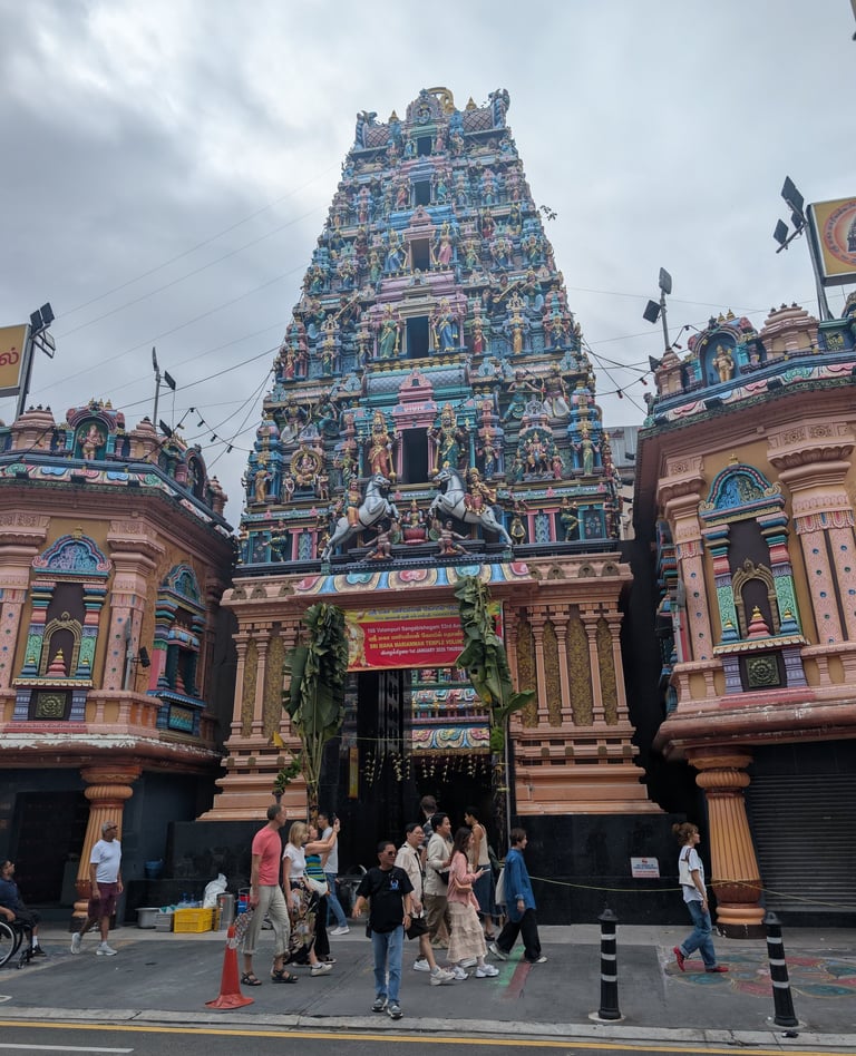 The colorful Dravidian architecture of Sri Mariamman Hindu Temple in Singapore with tourists walking past.