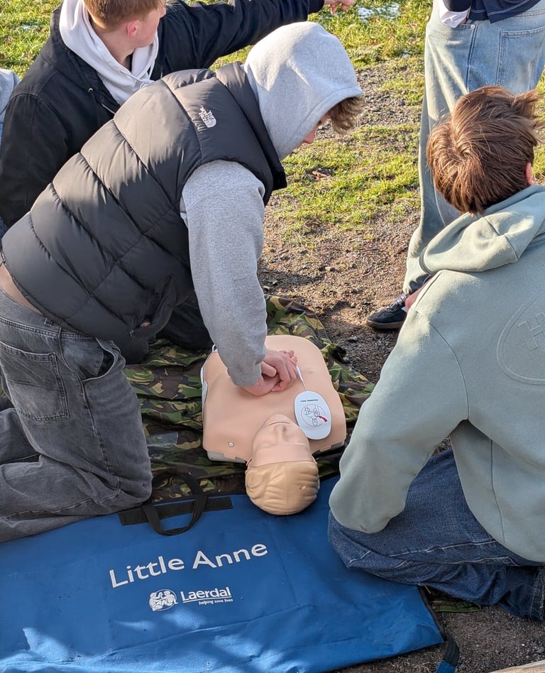 Students practicing outdoor CPR training using a Little Anne medical mannequin and AED pads.
