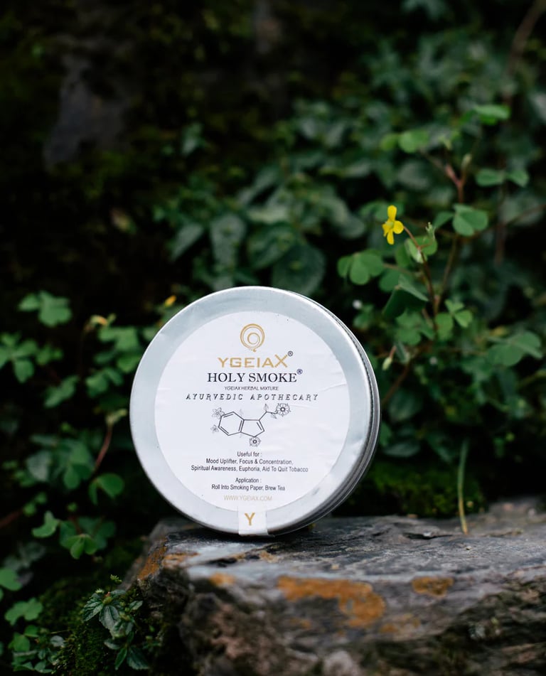 Ygeiax Holy Smoke Ayurvedic herbal mixture tin resting on a stone in a natural garden setting.