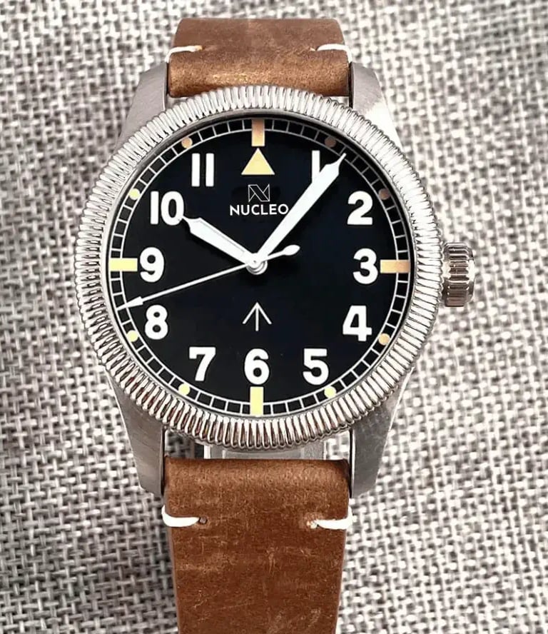 orologio militare field con lunetta fissa scanalata quadrante nero numeri arabi bianchi cinturino cuoio fondo tessuto grigio