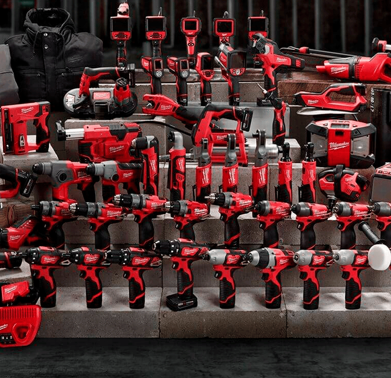 A wide assortment of red Milwaukee cordless power tools and heated gear displayed on concrete blocks.
