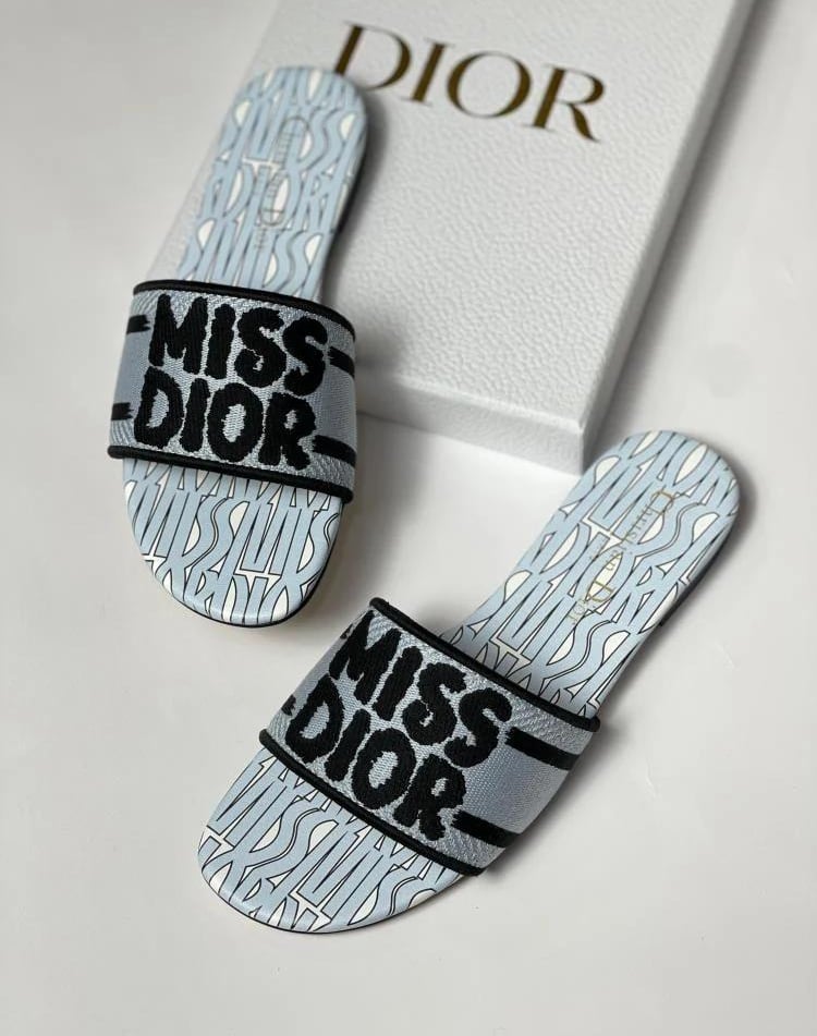Luxury Miss Dior flat slides in light blue and black embroidery next to a designer shoe box.