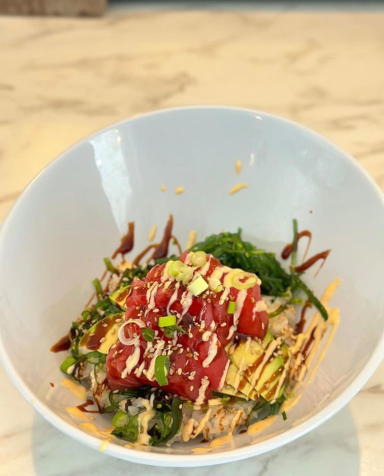 Fresh tuna poke bowl with avocado, seaweed salad, spicy mayo, and sesame seeds in a white bowl.