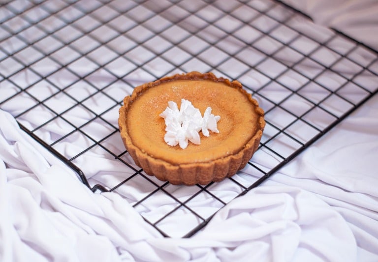 tartaleta mini de pay de queso con crema batida enfriándose sobre una rejilla negra de alambre.