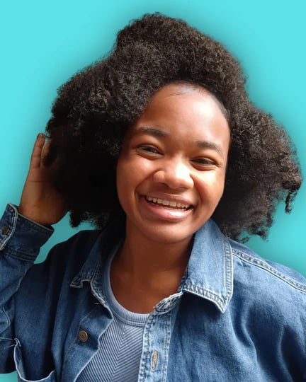 A smiling Black woman with voluminous natural hair wearing a denim jacket against a bright teal background.