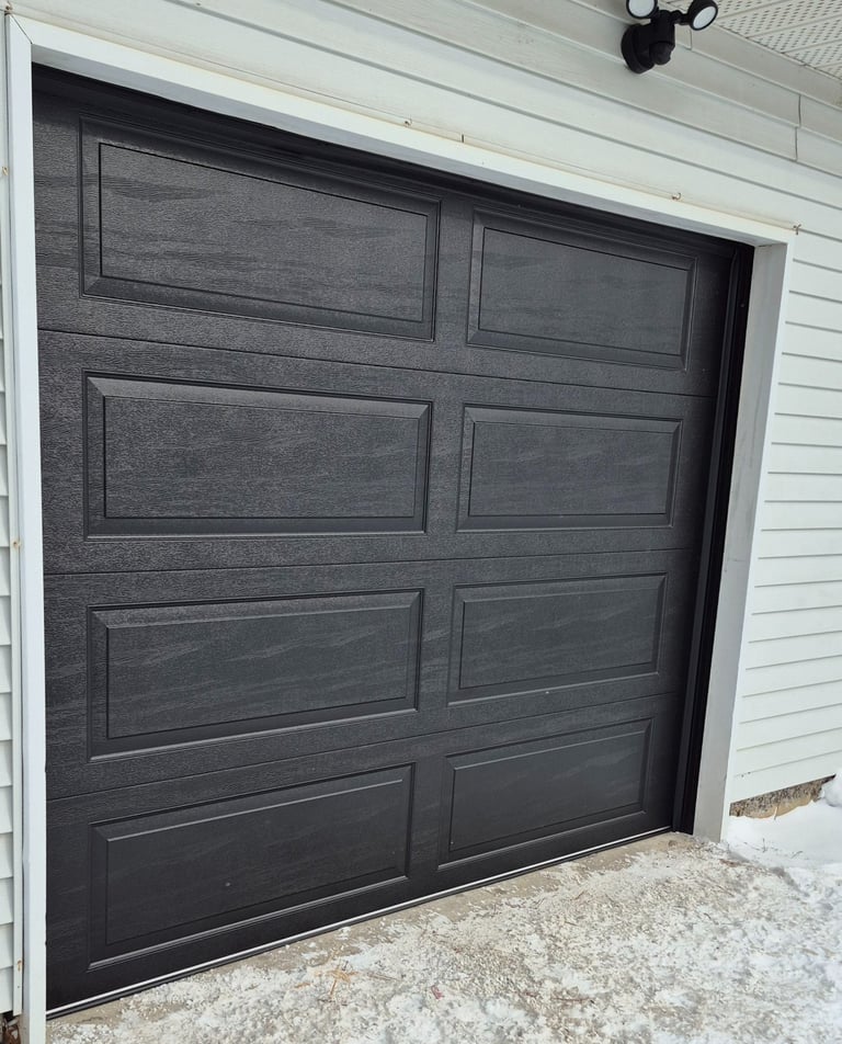 Modern black raised panel sectional garage door installed on a residential home with white siding.
