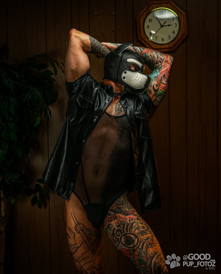 A tattooed man posing in a pup mask and leather vest.