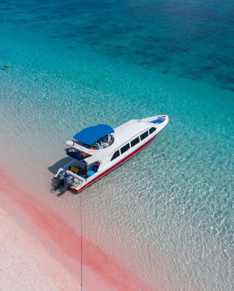 Colorful tour boats anchored at Pink Beach, Labuan Bajo, with bright turquoise waters and soft p