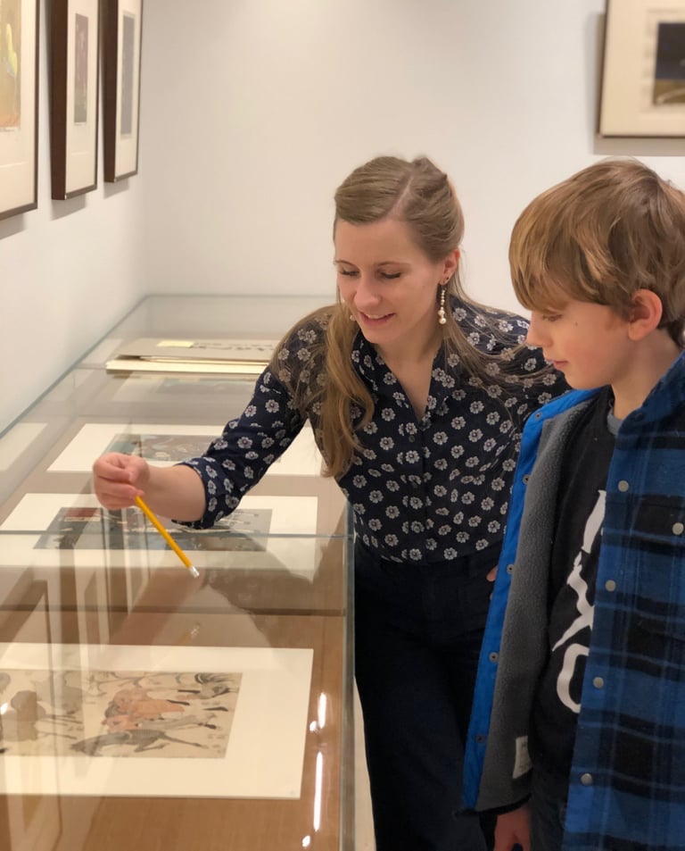 Madison points to a japanese print in the vitrine as she teaches a child in a gallery setting