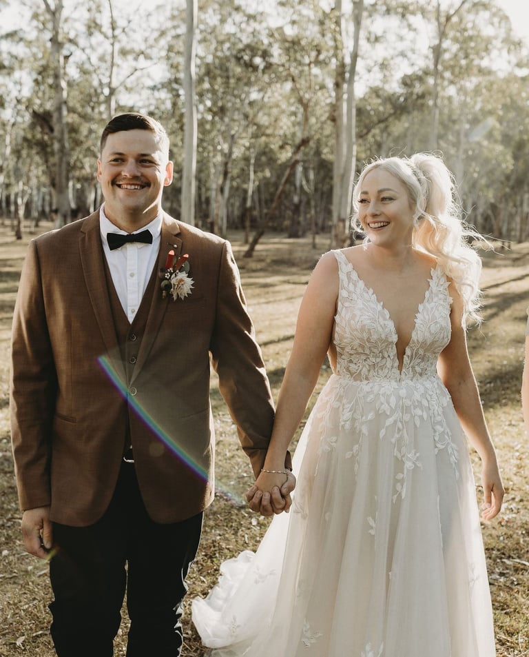 a bride and groom walking down a path in a wooded area