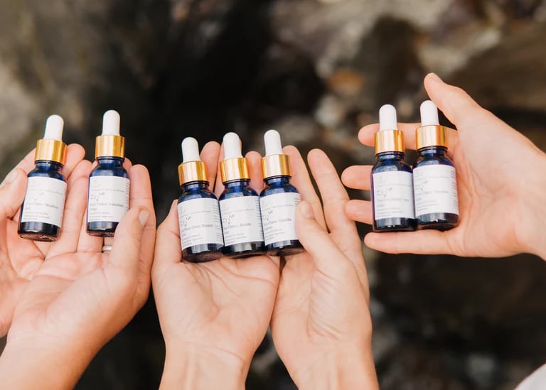 Hands holding blue glass dropper bottles of chakra essential oil blends against a natural stone background.