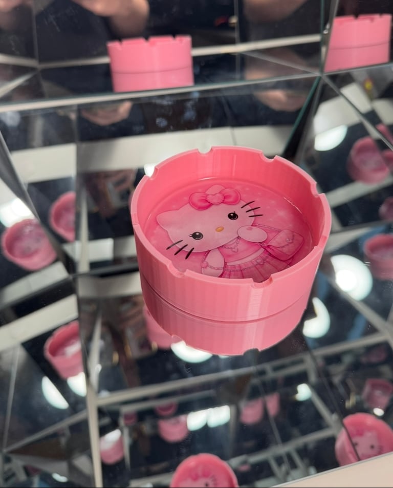 Pink Hello Kitty ashtray with character design on a mirrored surface reflecting multiple angles.