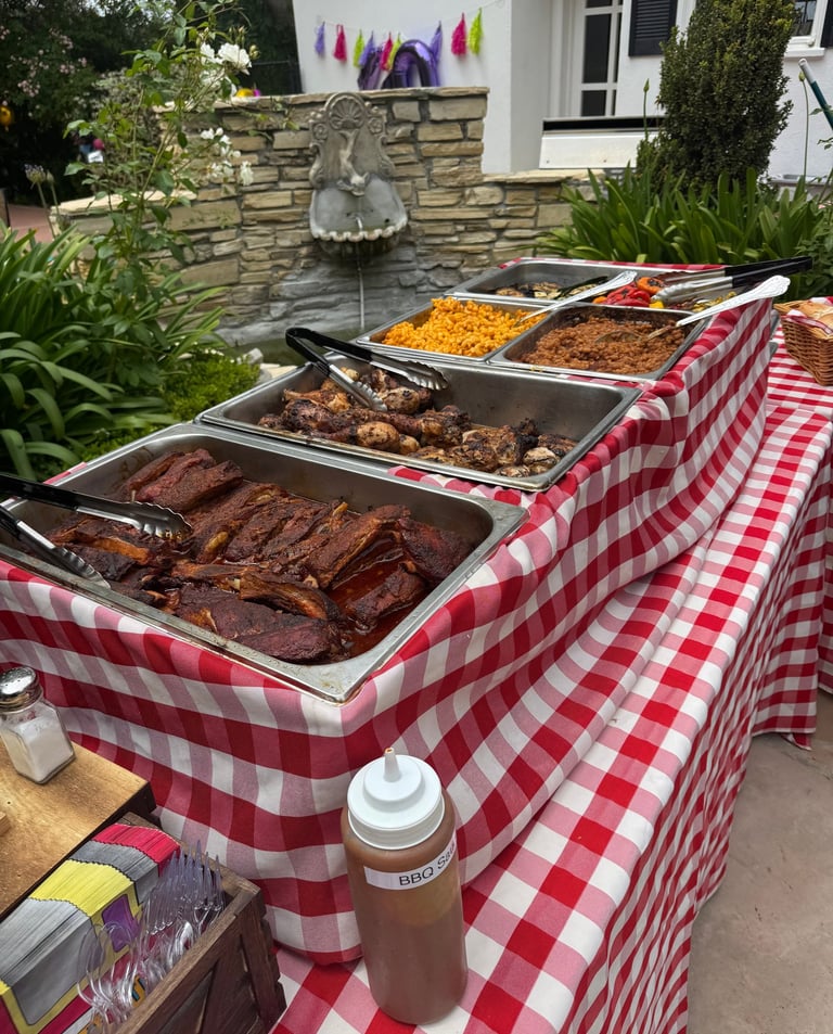 BBQ buffet setup with red checkered tablecloths, ribs, chicken, mac and cheese, and beans