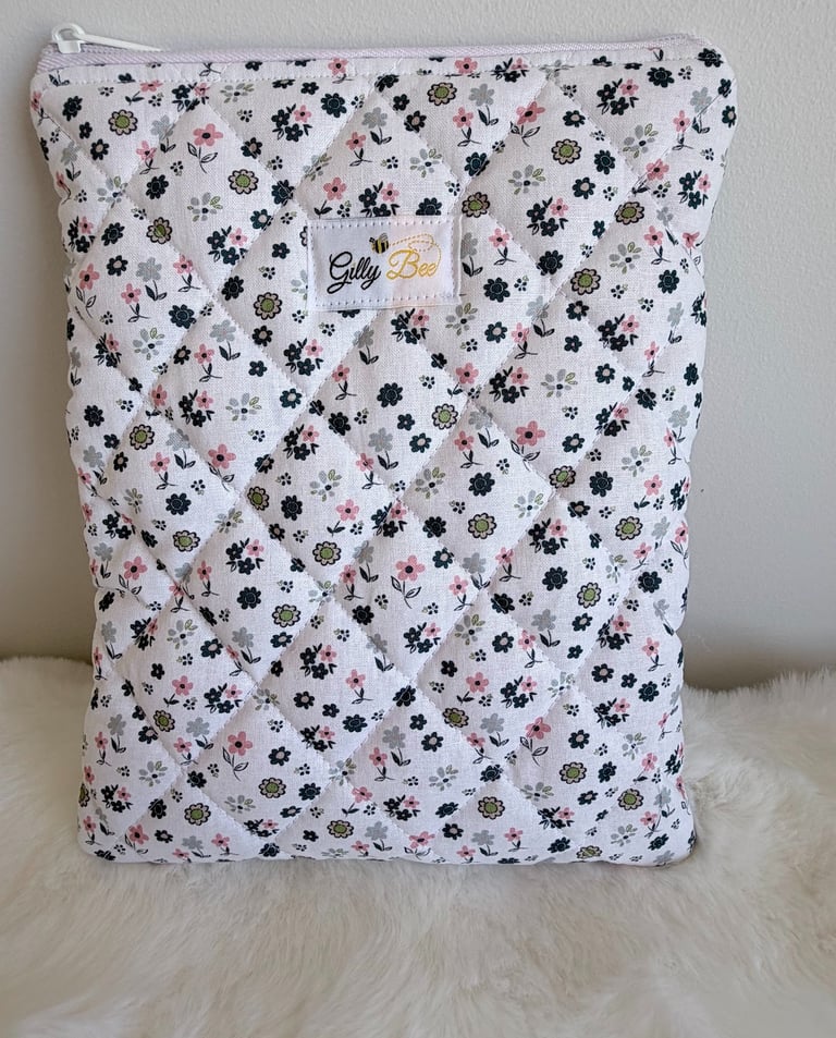 Quilted floral book sleeve with a zipper, featuring pink and green flowers on white fabric.