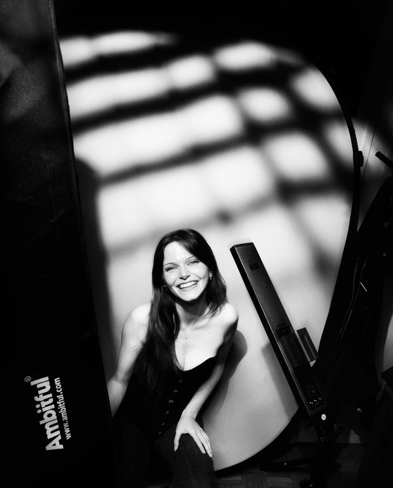 A smiling woman poses for a black and white studio portrait with dramatic gobo lighting patterns.