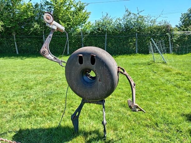 A creative metal sculpture of a character made from recycled scrap metal and car parts in a green field.