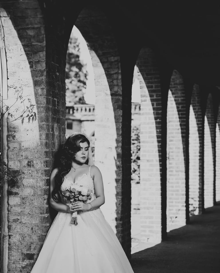 B&W portrait of a bride holding her bouquet under brick arches, photographed by Fred Art Studio.