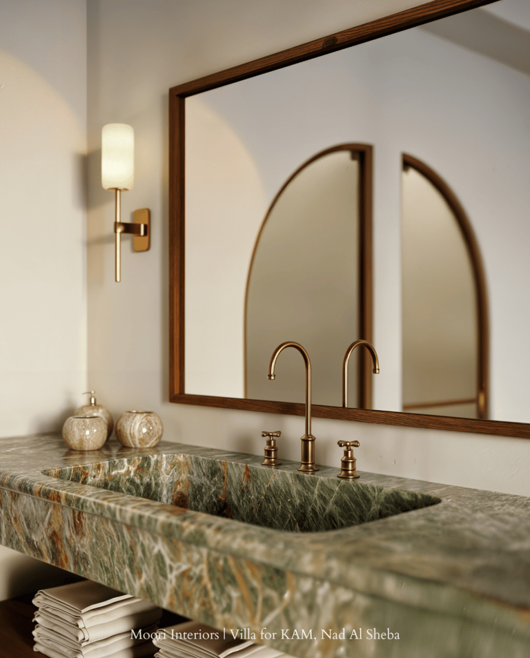 Close-up of green stone sink with bronze tap, wall sconce, and arched mirror reflection.