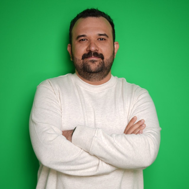 Portrait of a man with a mustache and beard in a white sweatshirt against a green background.