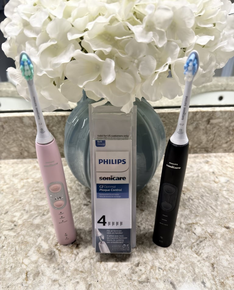 Two electric toothbrushes and open replacement head box on a clean bathroom counter with flowers