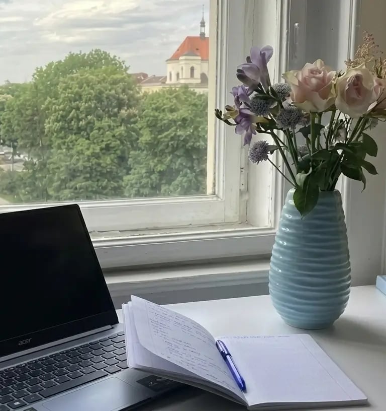 Espaço de trabalho sereno com luz natural suave, notebook aberto, caderno e vaso com flores 