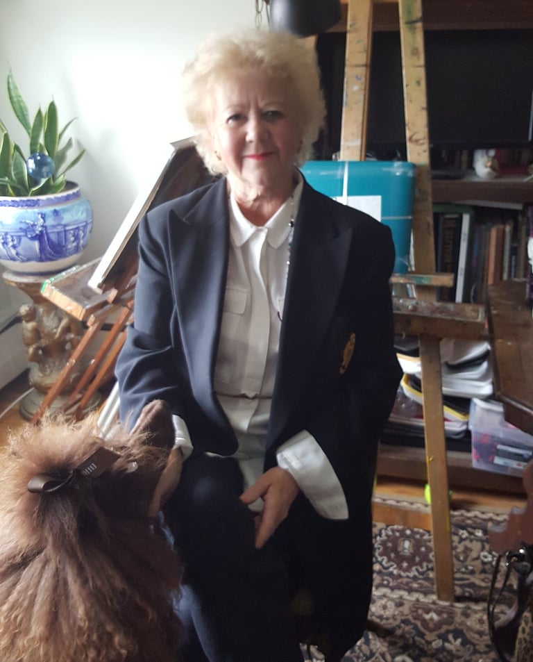 A picture of the artist sitting in her studio with an easel behind her.  