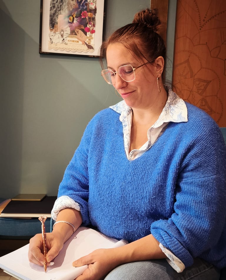 a woman in a blue sweater and glasses is writing on a notebook