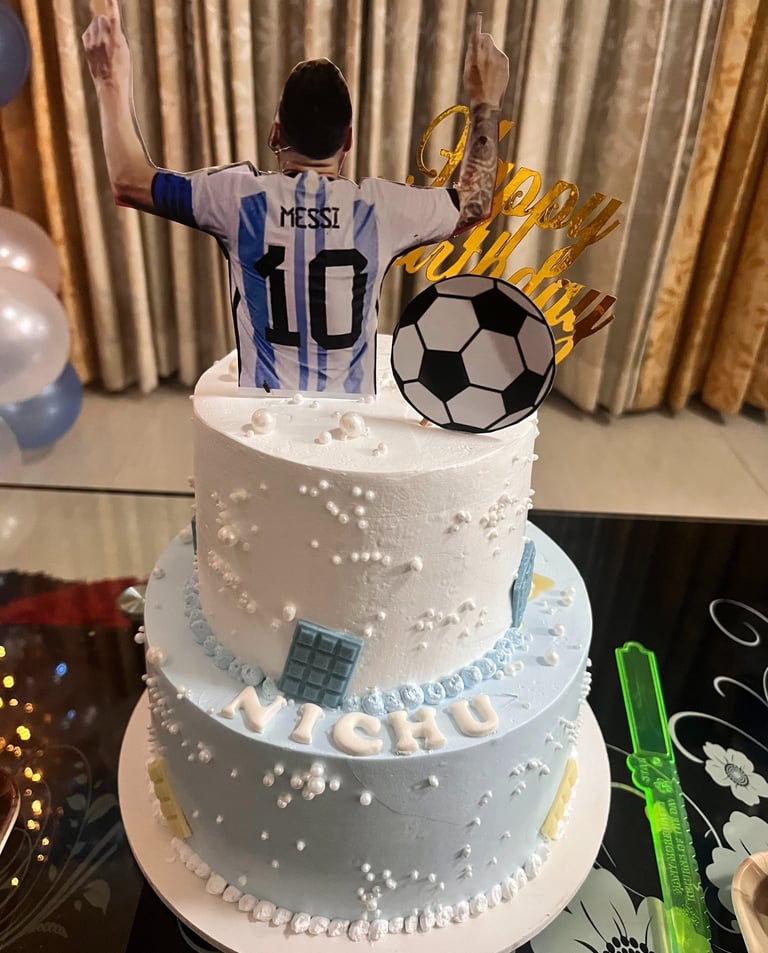 Lionel Messi themed two-tier birthday cake with soccer ball topper and Argentina jersey decoration.