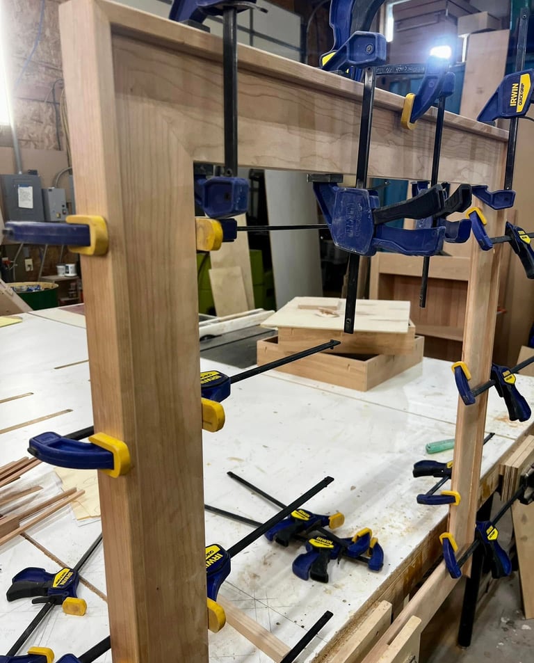 Wooden cabinet door frame being glued and secured with blue Irwin quick-grip clamps in a workshop.