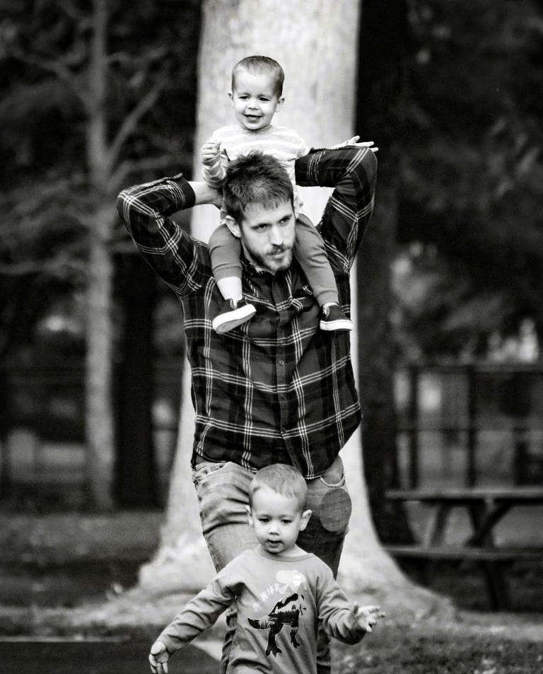 Father with one son on shoulders, other in front walking