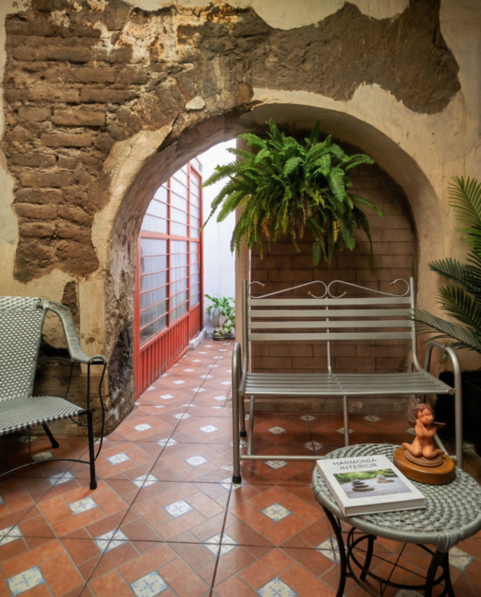 Encantador patio mexicano con entrada arqueada, piso de baldosas estampadas, sillas y plantas