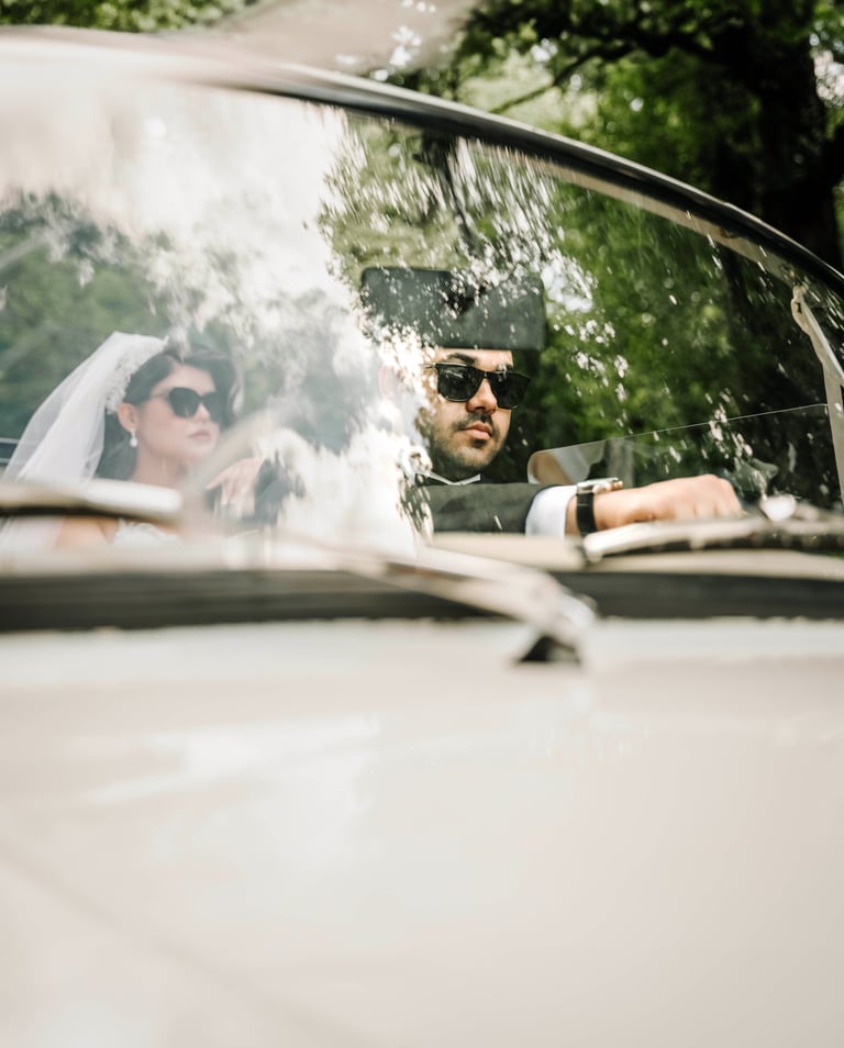 Bride and groom wearing sunglasses driving a classic car, captured by Fred Art Studio.