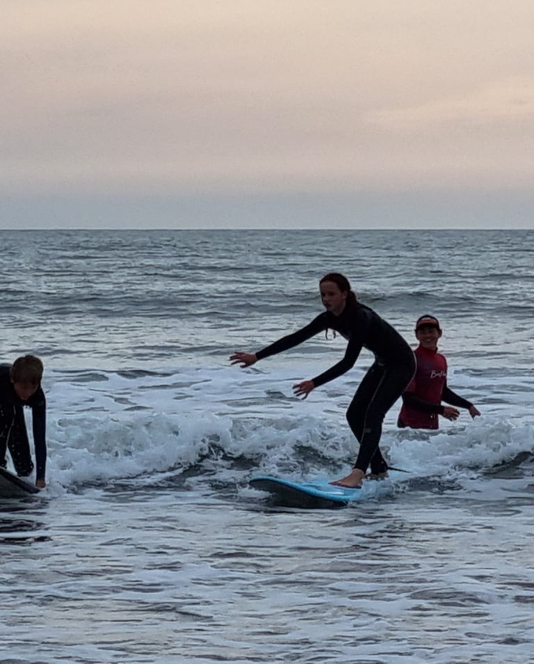 After school surf club lesson witha young female surfer riding a wave on a baby blue surfboard