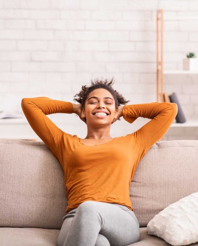 Smiling woman relaxing on a couch with her arms behind her head, enjoying a clean and tidy home envi