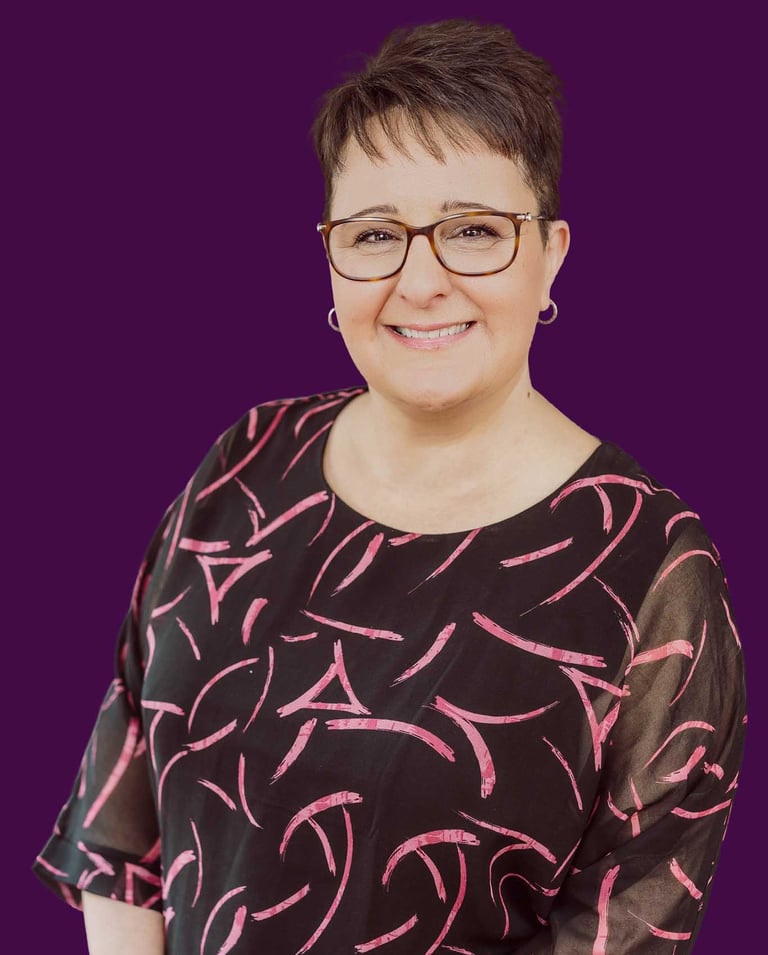 Professional portrait of a smiling woman with glasses and short hair on a purple background.
