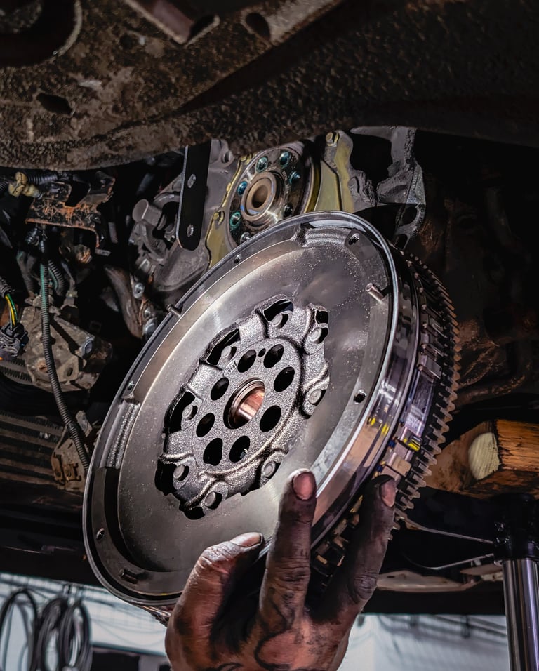 A mechanic holding a high-performance steel flywheel during a car clutch and transmission repair.