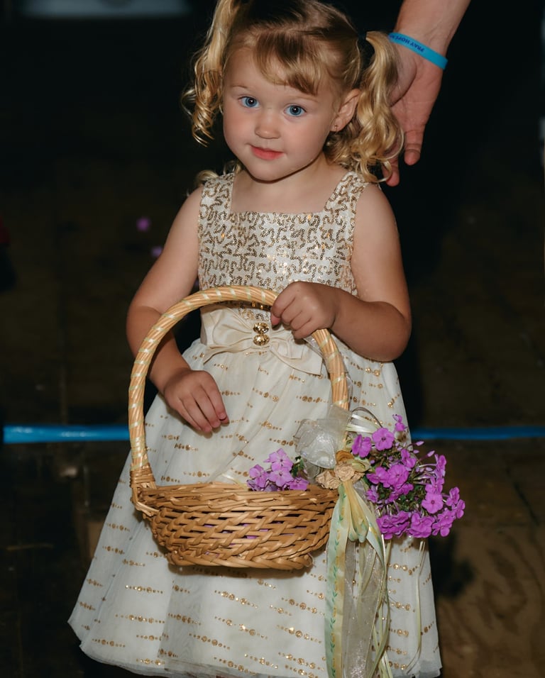 a little flower girl in a dress with a basket holding flowers
