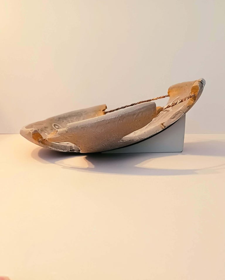 Side view of a bowl-like sculpture with embossed horse figures and symbols in rust/brown hues