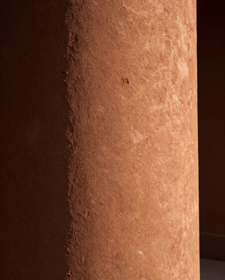 Close-up of a textured terracotta wall with raking warm light from the right edge, deep shadow to the left, architectural surface detail, cinematic stillness, no people