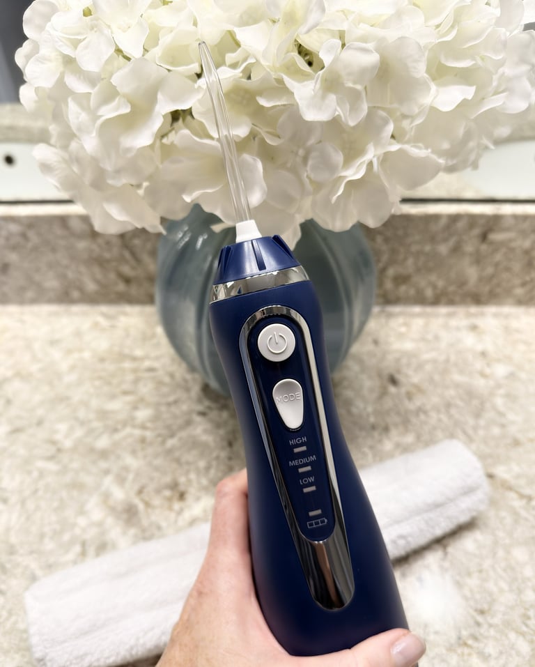 Christine holding a cordless water flosser with flowers and bathroom counter visible in background