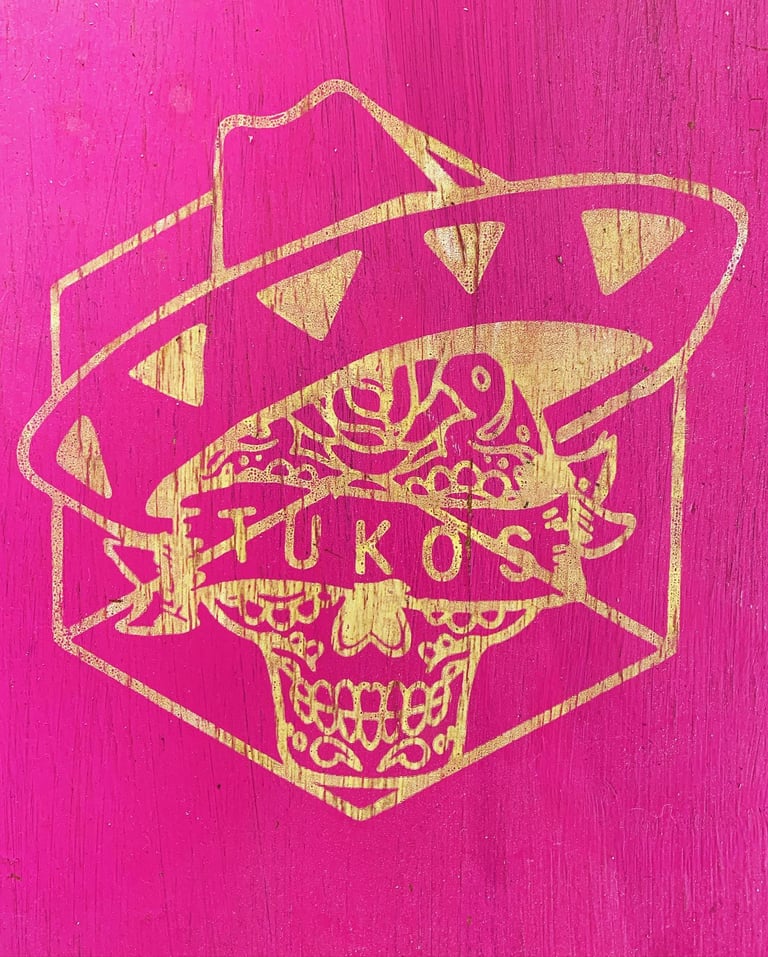 a pink and gold painted wooden sign with a mexican skull