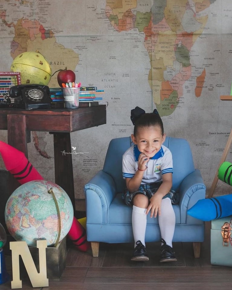 una niña pequeña en un set escolar, con un globo terráqueo y un mapa del mundo atrás de ella