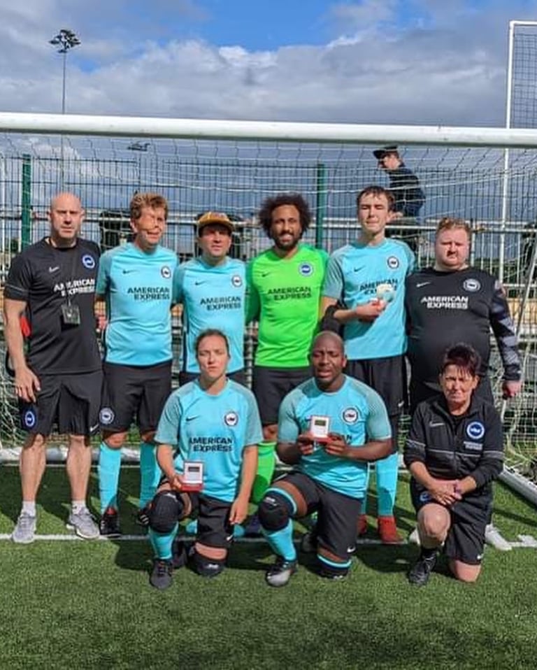 Group photo of a football team and staff standing in front of a goal on an artificial pitch.
