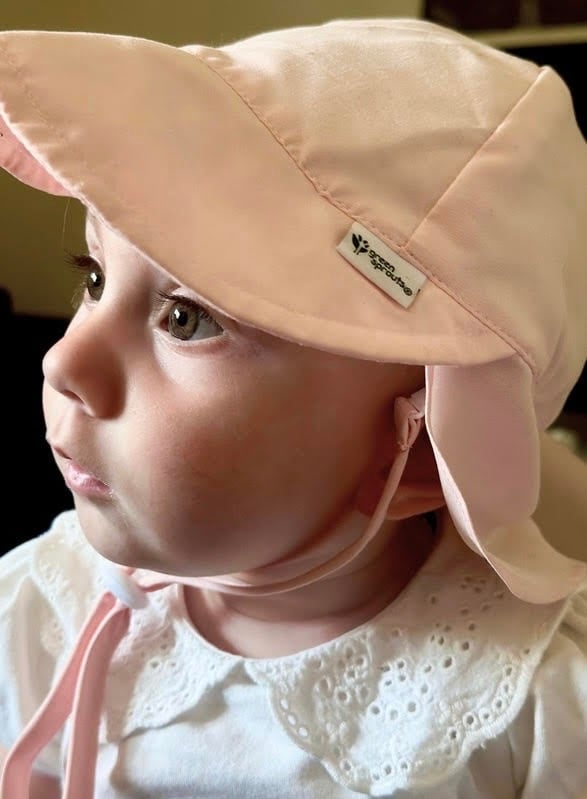 close-up profile of a baby wearing pink bucket hat, sunlight shining in her eyes and illuminating her face with a warm glow