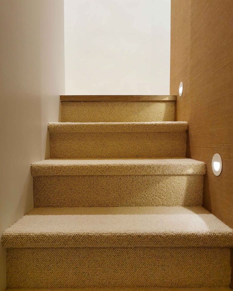 Modern indoor staircase with beige carpet runner and round LED recessed wall lights.