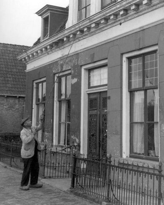Knocker-Upper em Londres, 1900, acordando cliente com vara na janela.