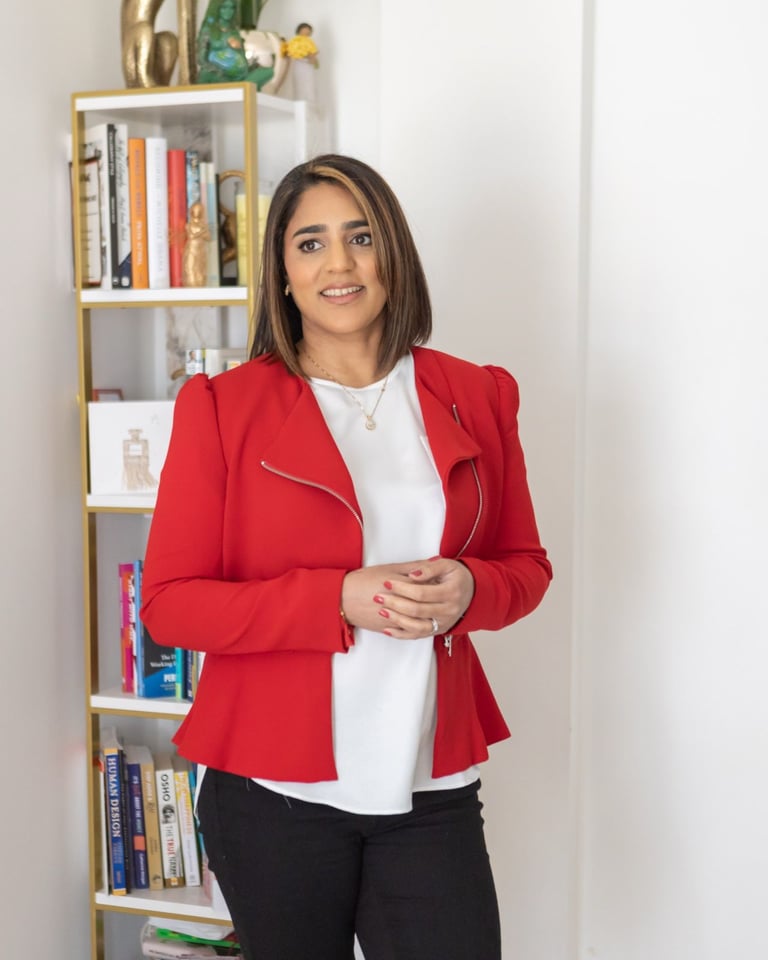 A photo of Anita wearing a white top, red jacket, and black trousers