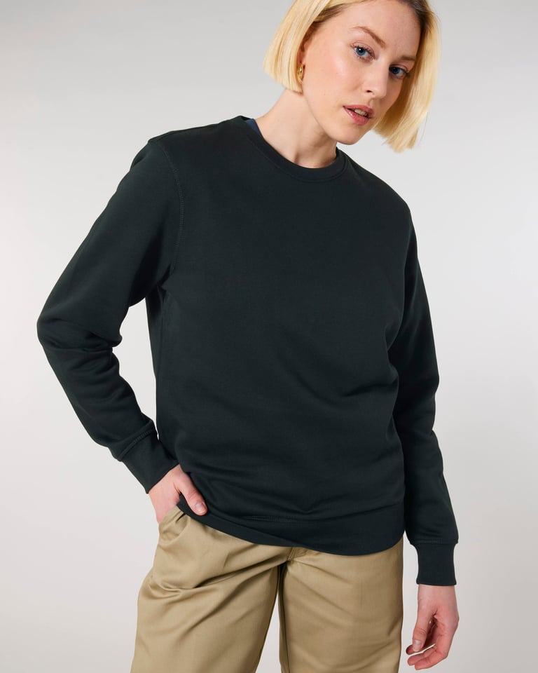 A blonde woman wearing a classic black crewneck sweatshirt and khaki pants against a white background.