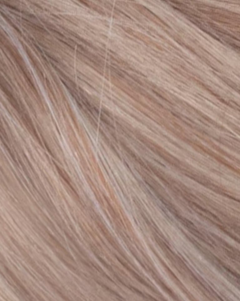 Gros plan de la texture de rallonges de cheveux blond fraise avec des mèches cendrées claires.