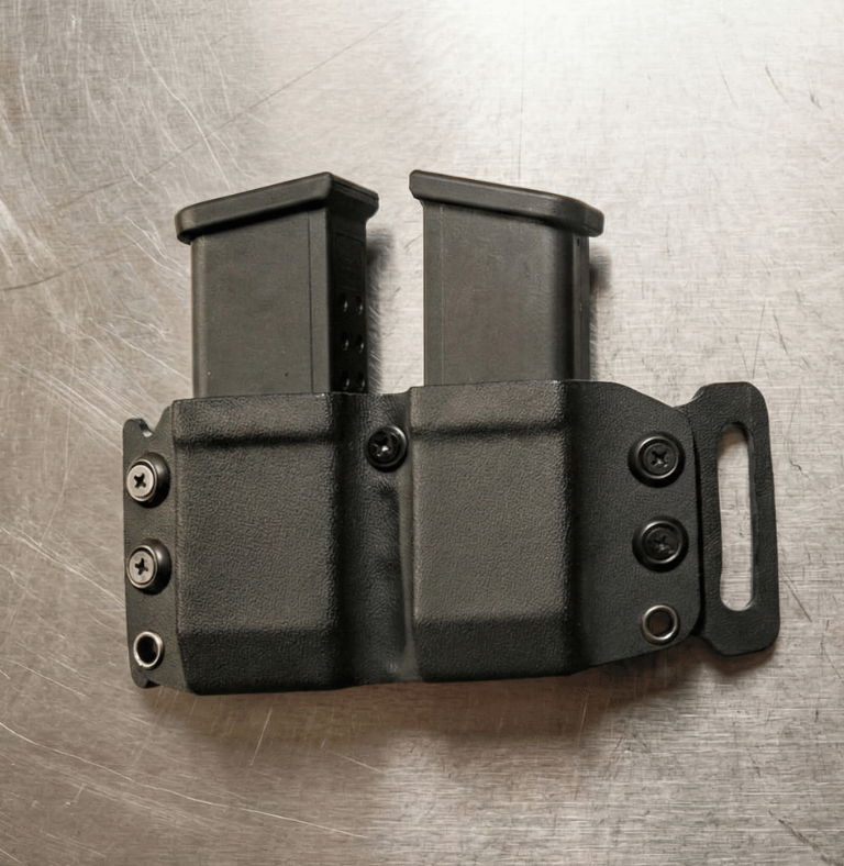 Black dual magazine pouch made of Kydex material holding two handgun magazines on a metal surface.